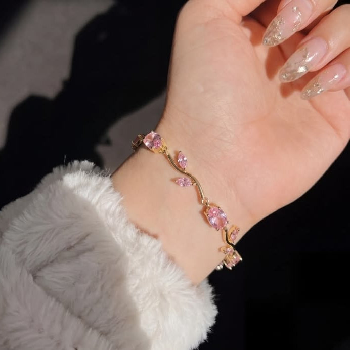 Hand wearing a delicate bracelet with pink stones against a dark background